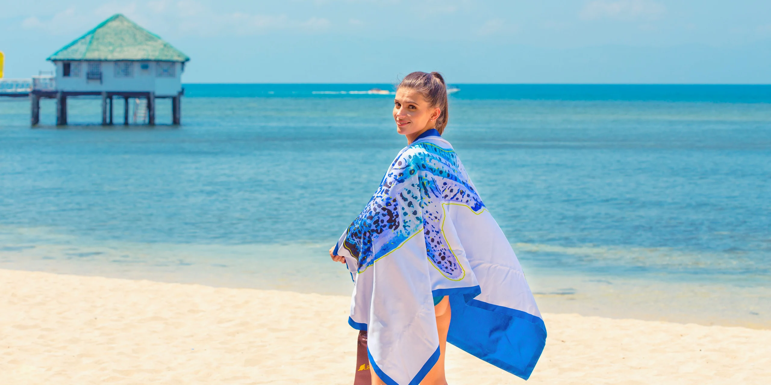 Model wrapped in the blue Peacock Pintados beach blanket beside the sea