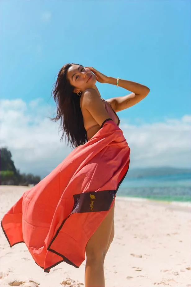 A beachgoer wearing an orange Lagu blanket in the sunshine